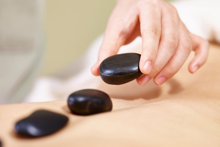 Eine Hand legt heiße, schwarze Steine auf einen Rücken