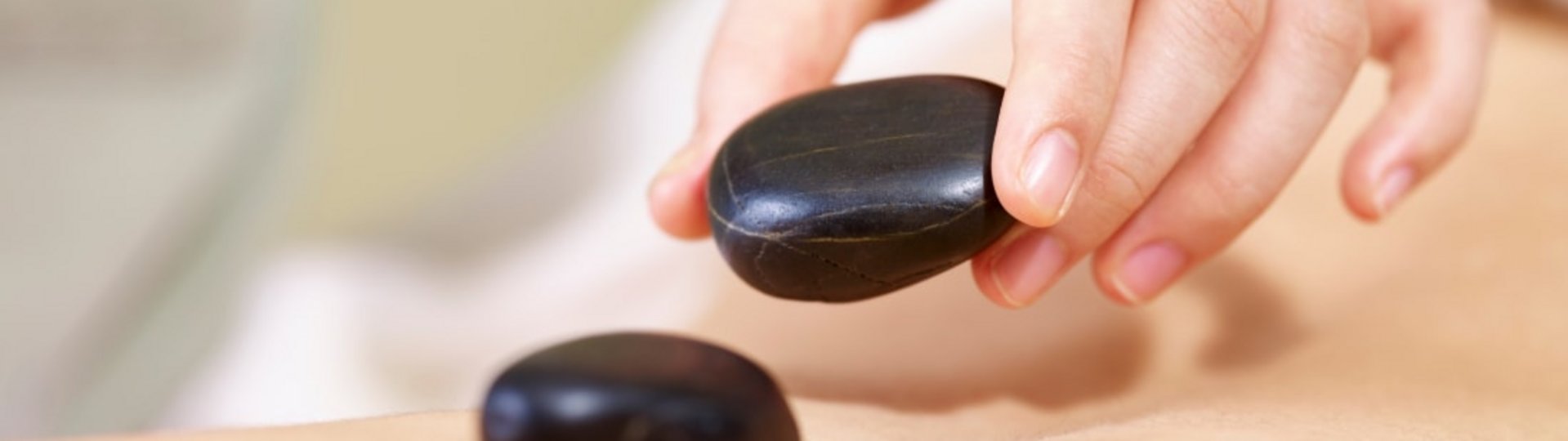 Eine Hand legt heiße, schwarze Steine auf einen Rücken