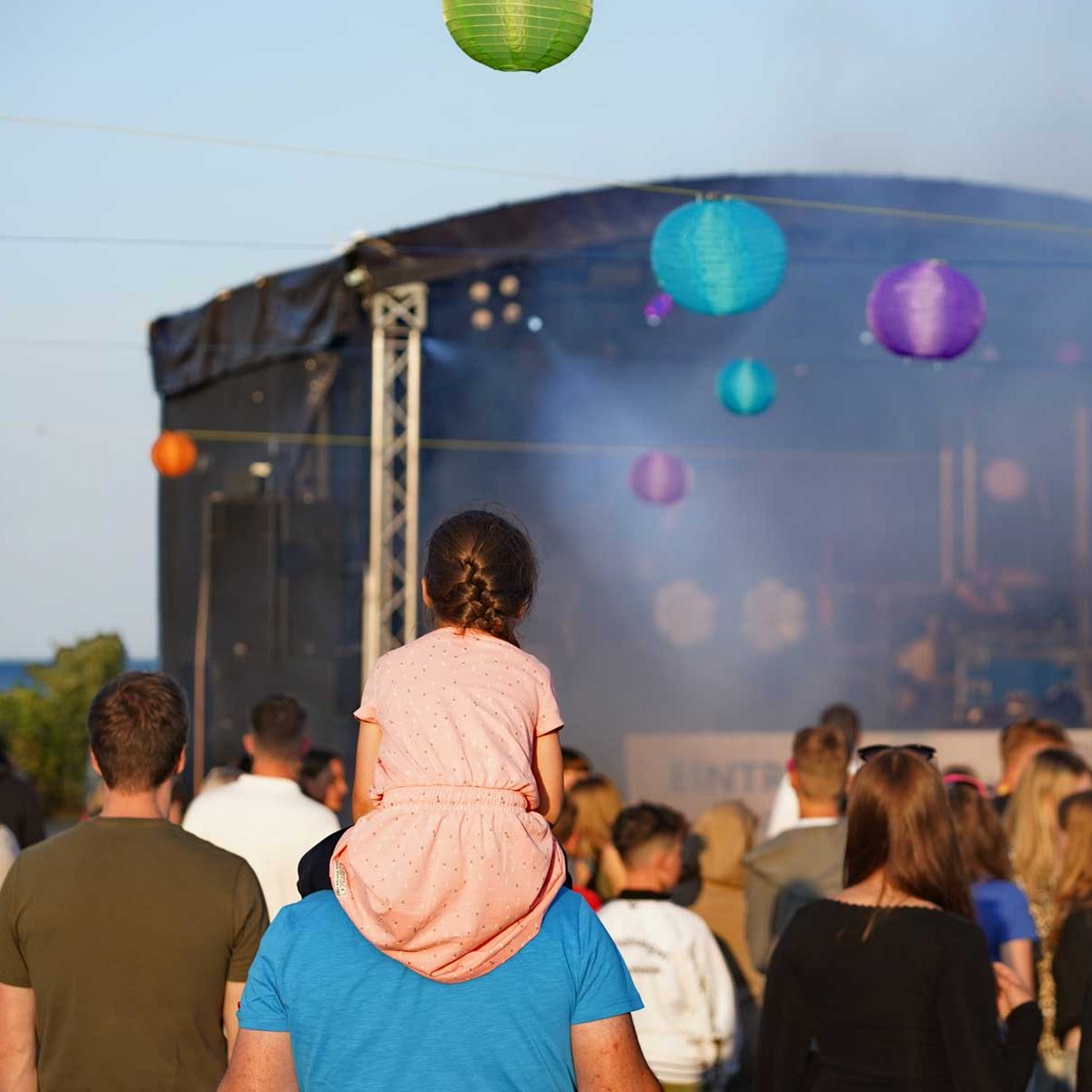 Eine Menschenmenge steht bei Tag vor einer Bühne, in der Luft schweben Ballons