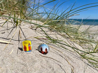 Zwei Plaketten für Wanderstöcke liegen am Strand in einer Düne