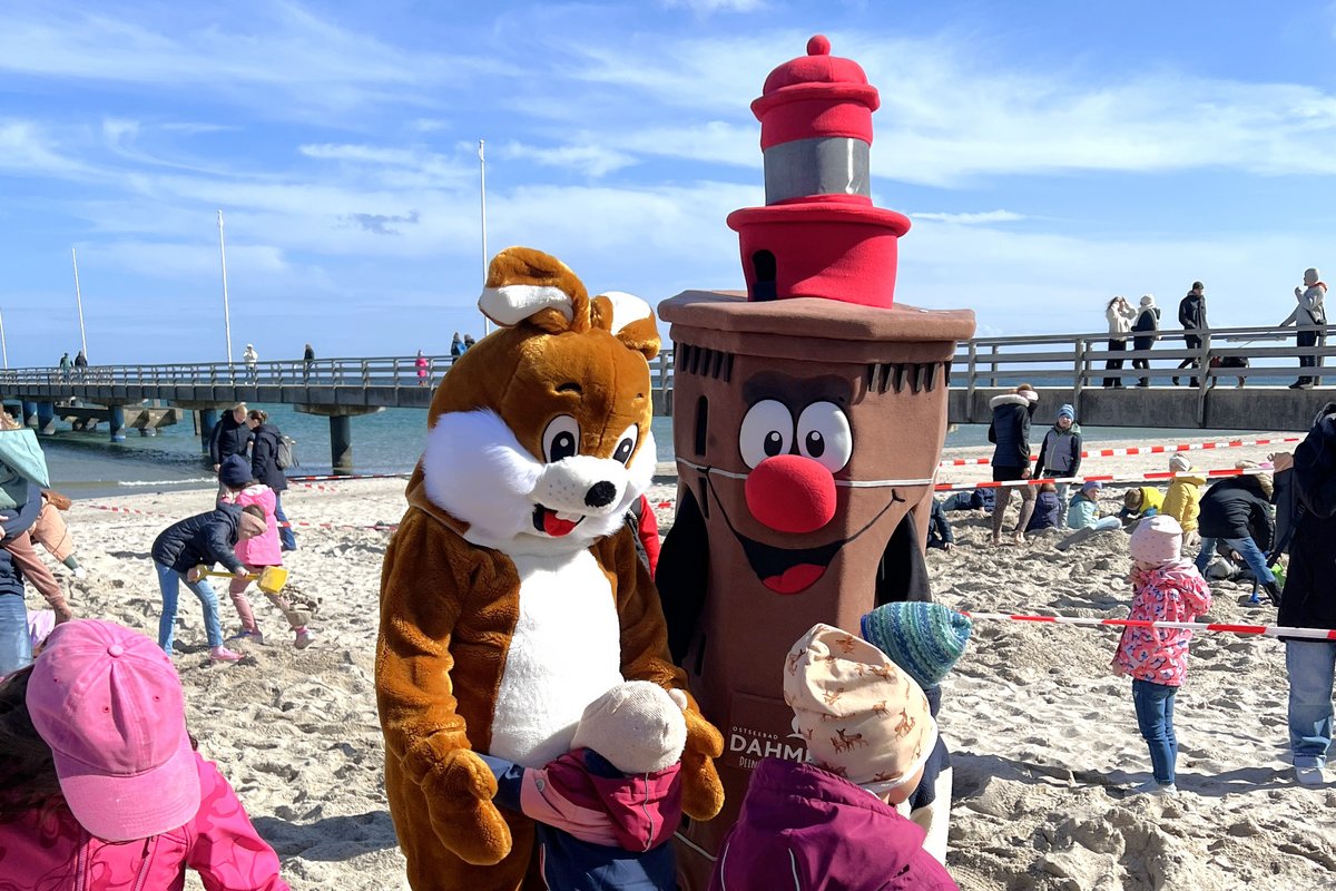Zwei Maskottchen (Osterhase und Leuchtturm) am Strand mit Kindern