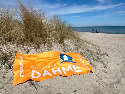 Ein oranges Badetuch liegt am Strand in einer Düne