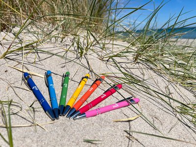 Bunte Kugelschreiber aus Plastik liegen am Strand in einer Düne