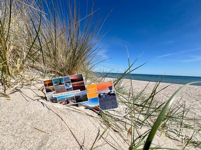Zwei Postkarten stecken am Strand in einer Düne