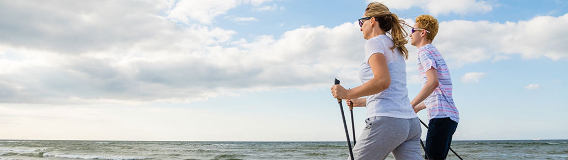 Eine Frau und ein junger Mann betreiben Nordic Walking am Strand