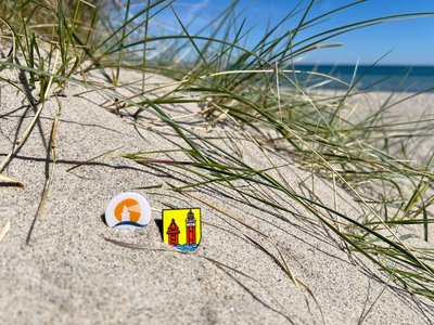 Zwei kleine Plaketten liegen am Strand in einer Düne