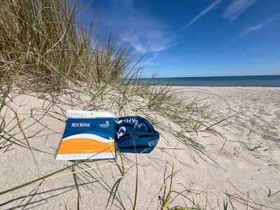 Ein Schlauchtuch liegt mit Verpackung am Strand in einer Düne