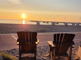 Zwei leere Holzsessel stehen bei Sonnenuntergang am Strand