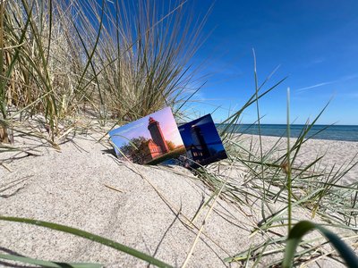 Zwei Postkarten stecken am Strand in einer Düne