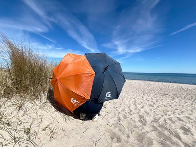 Zwei Regenschirme stehen am Strand in einer Düne