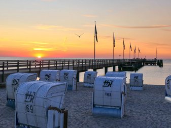 Ansicht der Seebrücke bei Dämmerung, im Vordergrund stehen weiße Strandkörbe