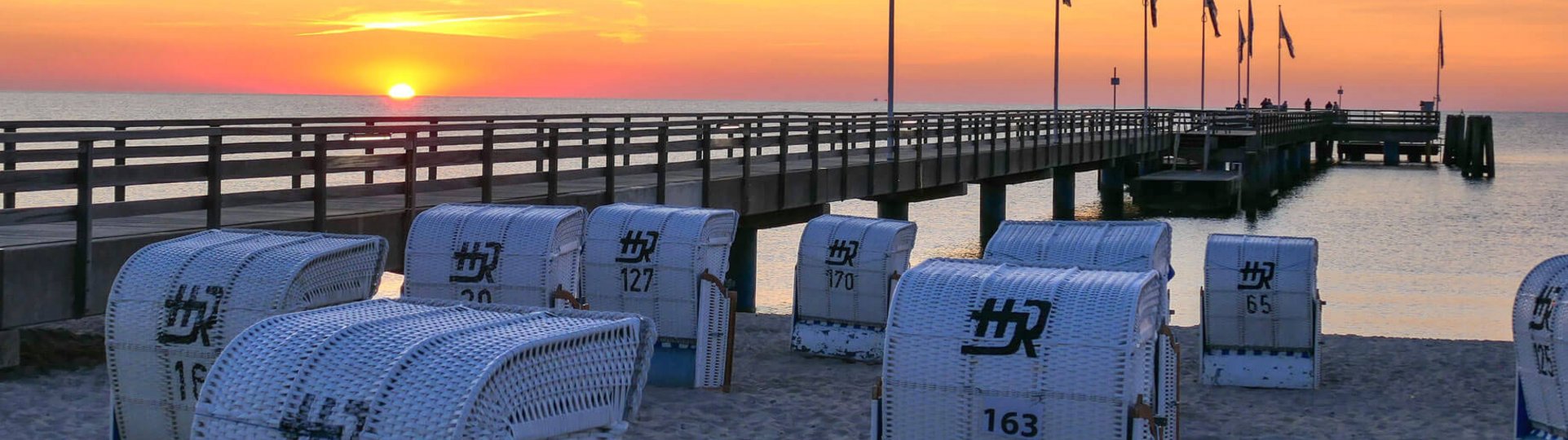 Ansicht der Seebrücke bei Dämmerung, im Vordergrund stehen weiße Strandkörbe