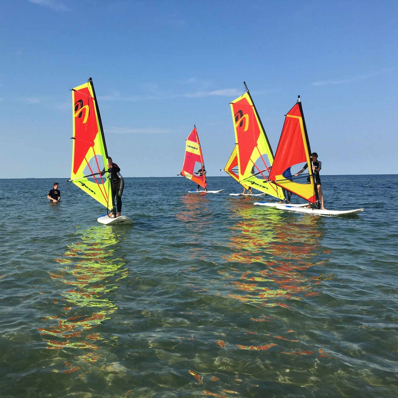 Eine Gruppe von Surfschülern mit rot-gelben Segeln lernt surfen