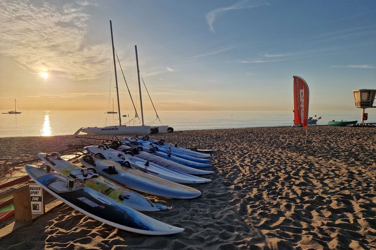 Mehrer Surfbretter liegen zum Trocknen am Strand, im Hintergrund geht die Sonne über dem Wasser unter