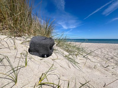 Eine graue Strickmütze liegt am Strand in einer Düne