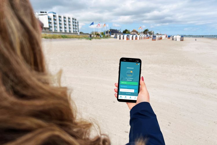 Eine Frau steht am Strand und betrachtet eine App auf ihrem Smartphone
