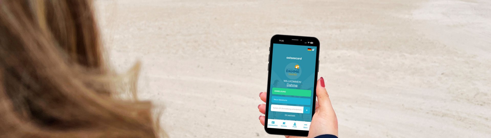 Eine Frau steht am Strand und betrachtet eine App auf ihrem Smartphone