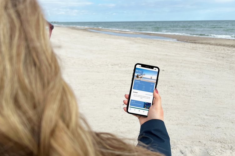 Eine blonde Frau betrachtet die App "Ostseeguide" auf ihrem Smartphone