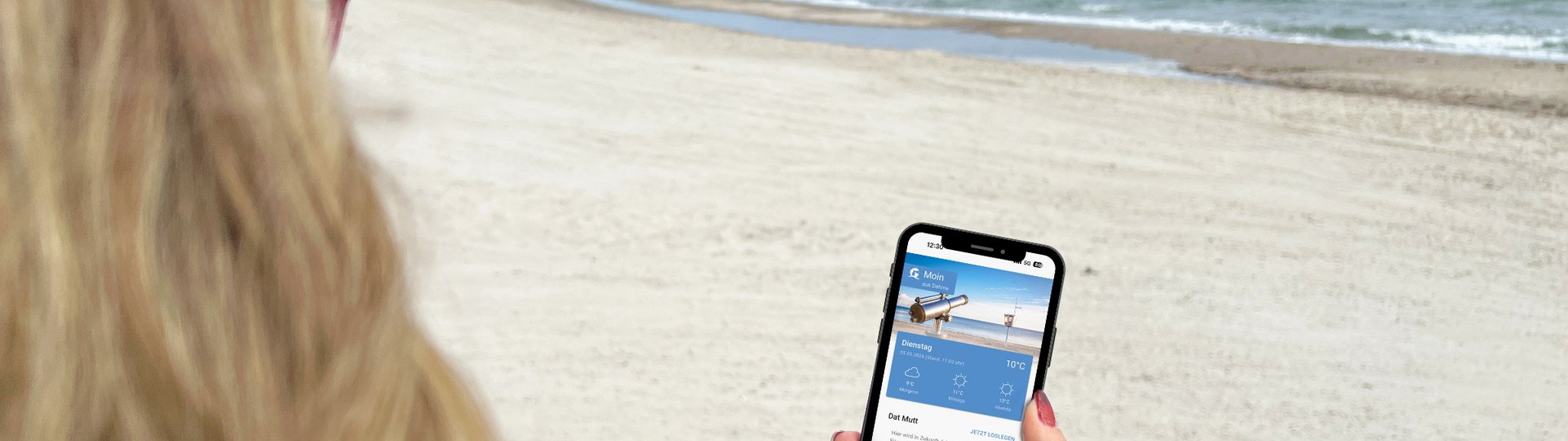 Eine blonde Frau betrachtet die App "Ostseeguide" auf ihrem Smartphone