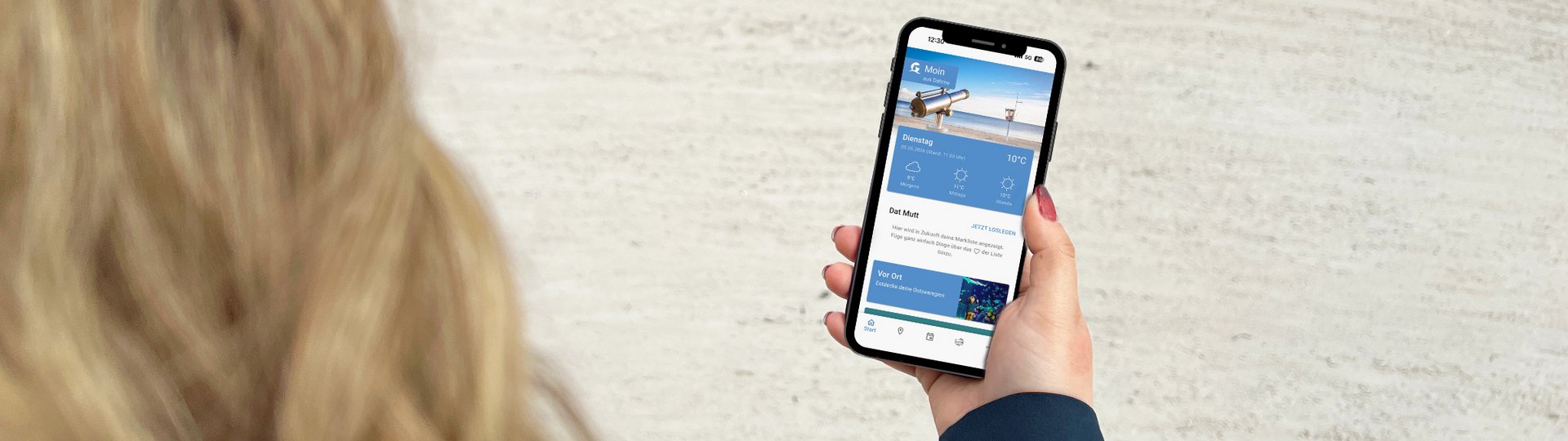Eine blonde Frau betrachtet die App "Ostseeguide" auf ihrem Smartphone