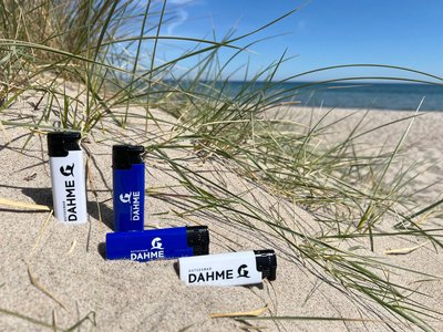 Mehrere Feuerzeuge aus Plastik liegen am Strand in einer Düne