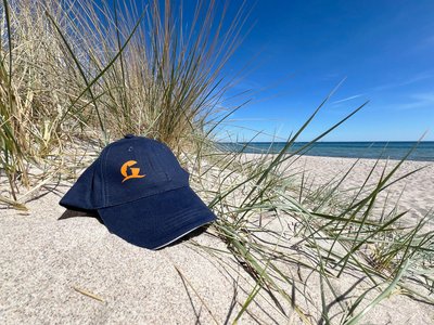 Eine blaue Basecap liegt am Strand in einer Düne